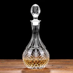 an empty glass decanter sitting on a wooden table with a black back ground