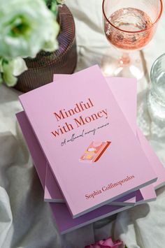 two pink books sitting on top of each other next to a wine glass and flowers