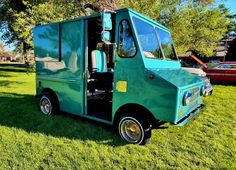 a green food truck parked on top of a lush green field next to a red car