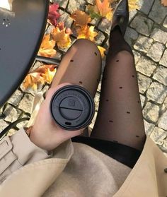 a woman is sitting on the ground with her legs crossed and holding a coffee cup