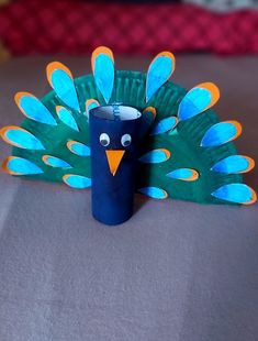 a peacock made out of paper sitting on top of a bed next to a cup