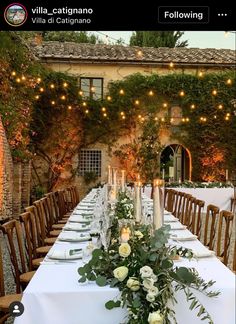 a long table with candles and flowers on it in front of an old building at night