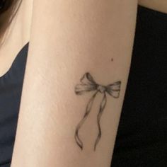 a woman's arm with a bow tattoo on the left side of her arm