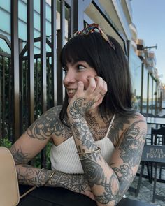 a woman sitting at a table with tattoos on her arms and legs, talking on the phone