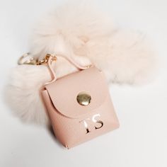 a pink handbag with a fur ball on the side and a keychain attached to it