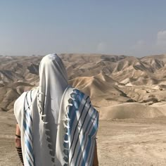 a person wearing a white and blue striped shawl looking out over the desert hills