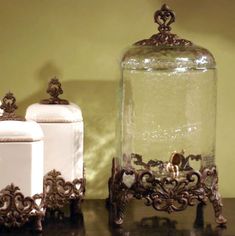 an ornate glass jar and two white ceramic containers on a black table with a yellow wall in the background