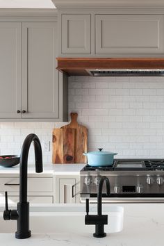 a kitchen with gray cabinets and black faucets on the counter top, along with an oven hood