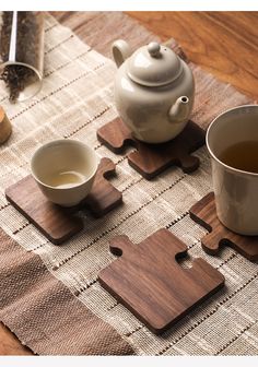 a tea set on a table with two cups and one piece of wooden puzzle sitting next to it