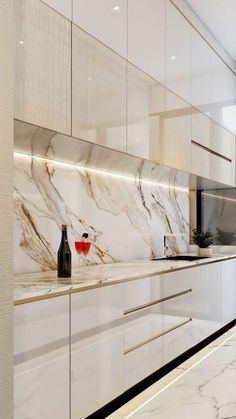 a kitchen with marble counter tops and white cabinets, along with a wine bottle on the counter