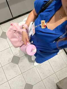 a woman in blue scrubs her hands on a pink object while standing next to a tiled floor