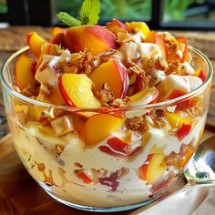 a glass bowl filled with fruit salad on top of a wooden table next to a spoon