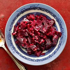 a bowl filled with beets on top of a red table next to a spoon