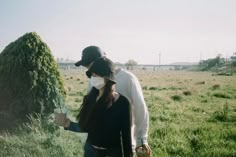 a man and woman walking through a field wearing face masks while holding coffee cups in their hands