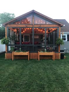 a backyard covered in lights and plants with benches on the grass next to an outdoor kitchen