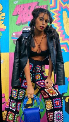 a woman sitting on top of a colorful wall holding a blue handbag in front of her face