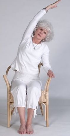 an older woman sitting in a chair with her arms stretched out to the side while stretching