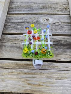 an image of a glass object with flowers and grass in it on a wooden surface