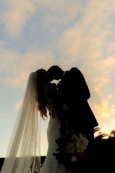 a bride and groom kissing in front of the sunset