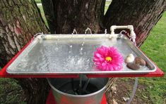 a pink flower sitting on top of a metal tray next to a red trash can