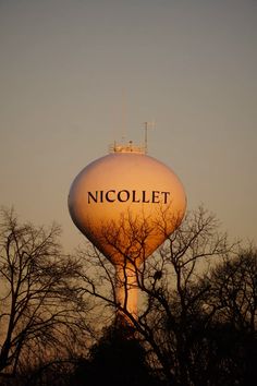 a water tower with the word nicollet on it's side at sunset