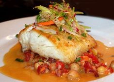 a white plate topped with fish covered in sauce and garnished with veggies