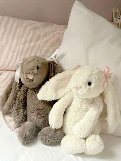 two stuffed animals sitting next to each other on a bed