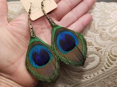 a pair of peacock feather earrings on a person's hand with a tag in the background