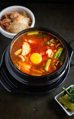 a bowl of soup with meat and vegetables next to another bowl of food on the table