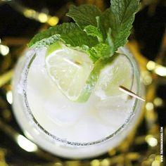 a close up of a drink in a glass with limes and mint on the rim