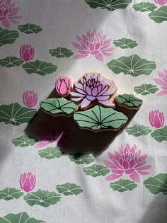 there is a pink and green flower on top of a white table cloth with water lilies