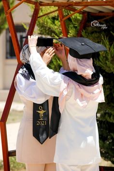 two people in graduation gowns are taking pictures with their cell phones while standing under a gazebo