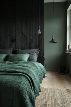 a bed with green sheets and pillows in a dark room next to a large window