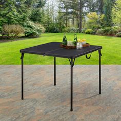 a black table sitting on top of a patio next to a lush green field with trees