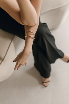 a woman sitting on top of a white couch with her legs crossed and wearing gold bracelets