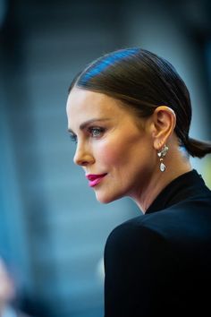 a woman with dark hair wearing earrings and a black top is looking off to the side