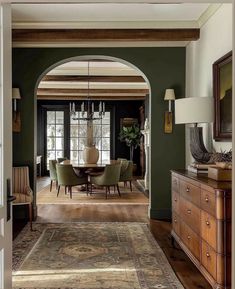 a dining room with green walls and wooden floors, an archway leading to the living room