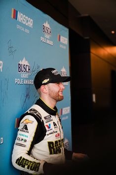 a man in a racing uniform standing next to a blue wall with autographs on it