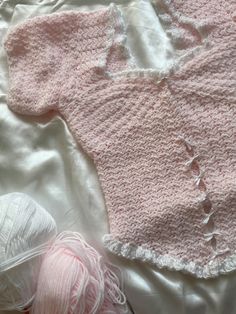 two balls of yarn sit next to a pink sweater and ball of thread on a white sheet