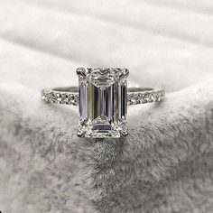 an emerald - cut diamond ring sits on a white blanket