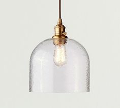 a clear glass pendant light hanging from a ceiling fixture with a gold finish on the top