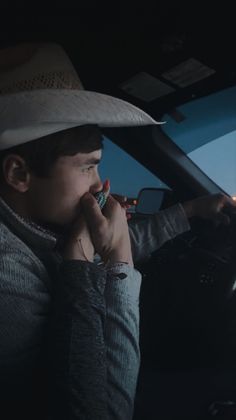 a man wearing a hat talking on a cell phone in the passenger seat of a car