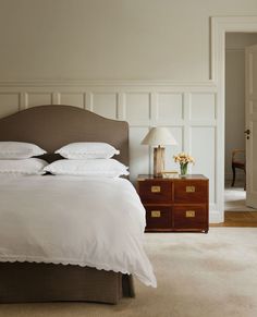 a bed with white linens and pillows in a bedroom next to a wooden dresser