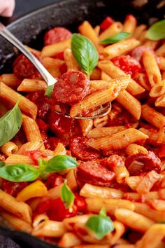 pasta with tomato sauce and basil leaves in a skillet being held by a spoon