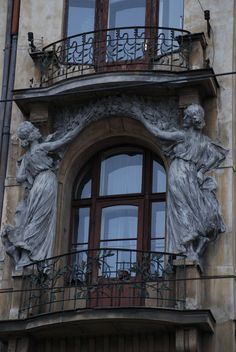 two statues on the side of a building next to an open window with shutters