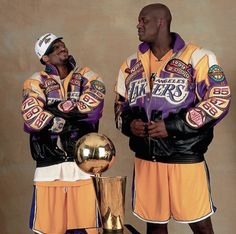 two men standing next to each other in front of a golden trophy and basketball ball