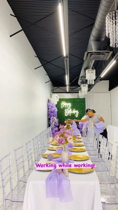 a long table with white chairs and purple flowers on it is set up for an event