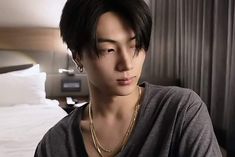 a young man with black hair wearing a gray shirt and gold necklace in a hotel room