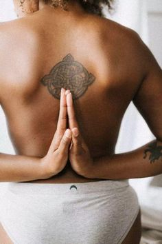 a woman with tattoos on her back is sitting in a yoga position and holding her hands together