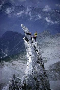 a man sitting on top of a rock next to a tall mountain under a cloudy sky